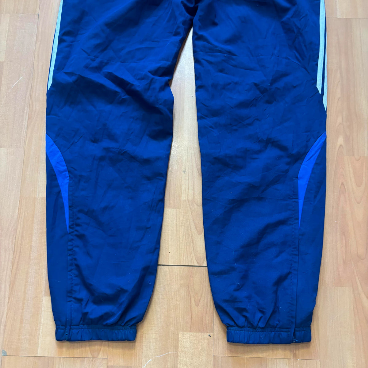 Adidas blue joggers with white three stripes, elastic waist, and ankle zips.