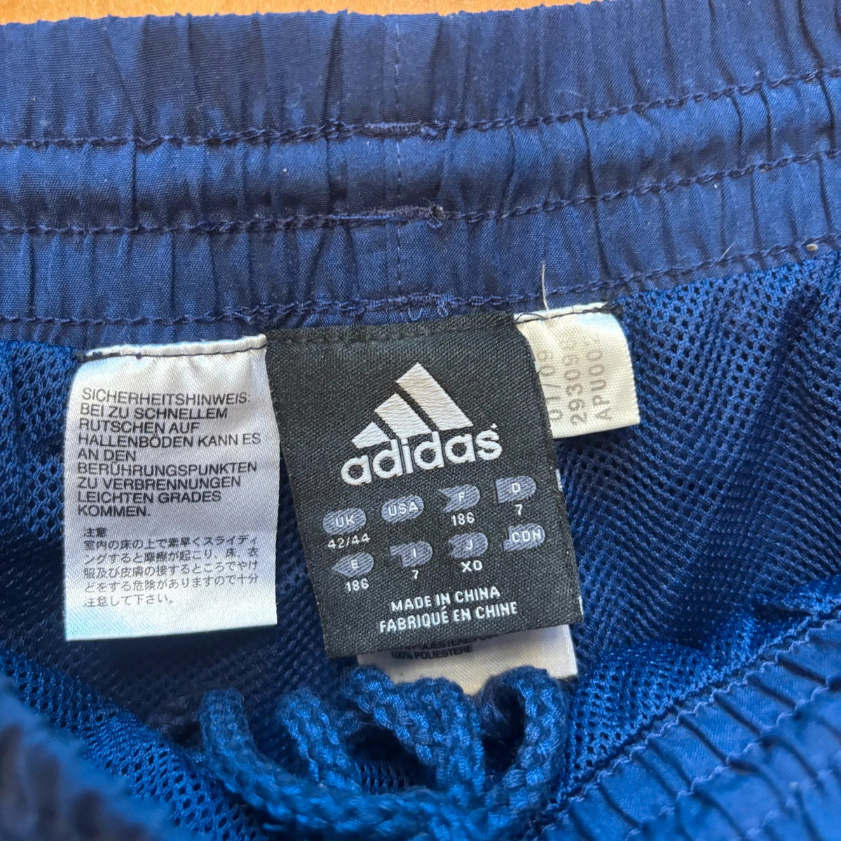 Adidas blue joggers with white three stripes, elastic waist, and ankle zips.