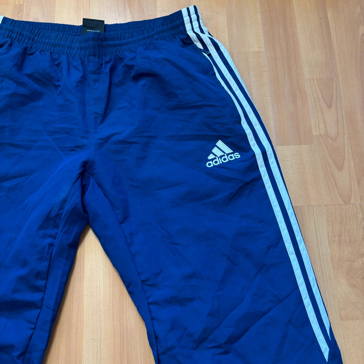 Adidas blue joggers with white three stripes, elastic waist, and ankle zips.