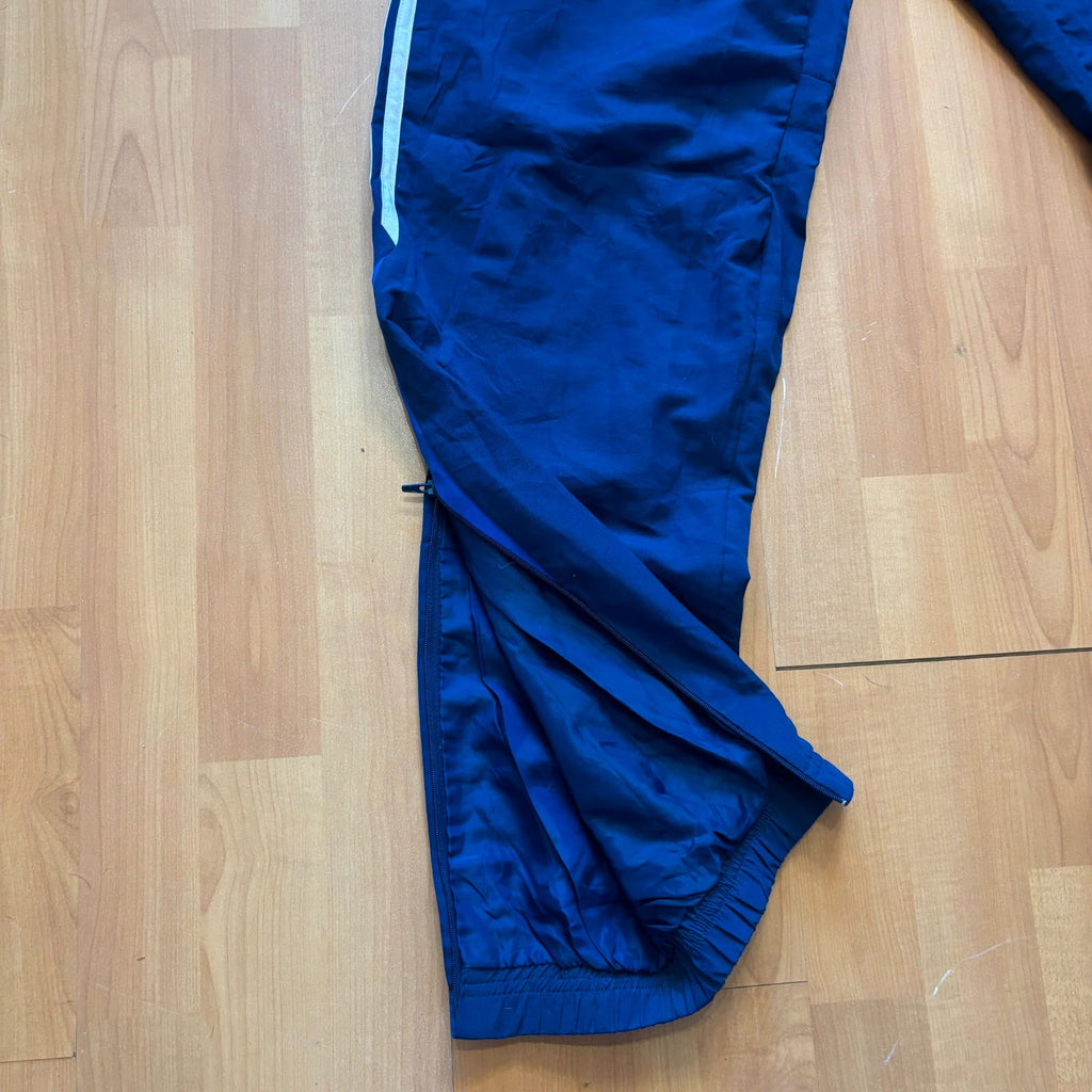 Adidas blue joggers with white three stripes, elastic waist, and ankle zips.