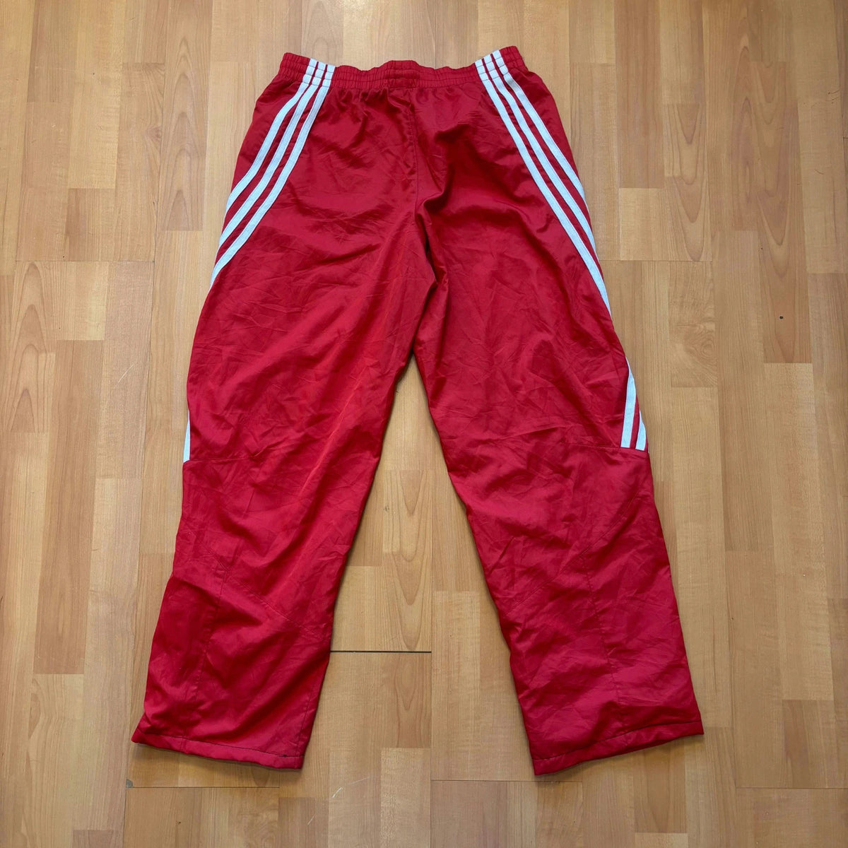Adidas red joggers with white three-stripe detailing and adjustable drawstring waist.