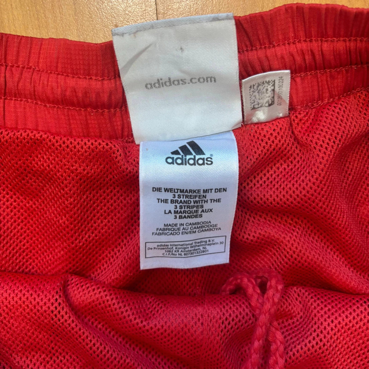 Adidas red joggers with white three-stripe detailing and adjustable drawstring waist.