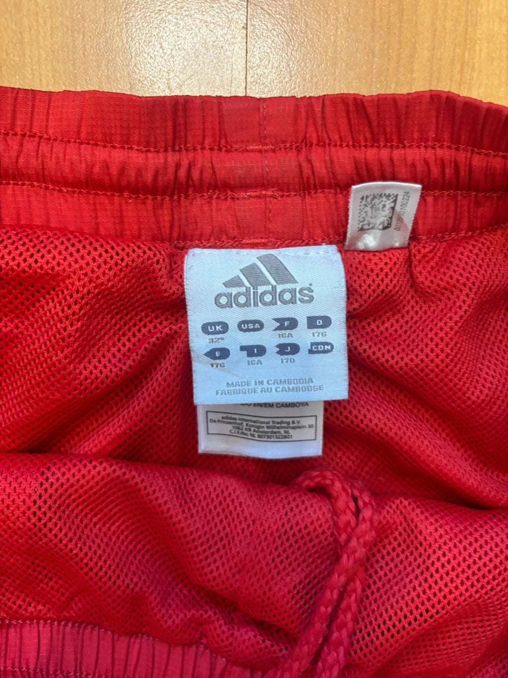 Adidas red joggers with white three-stripe detailing and adjustable drawstring waist.
