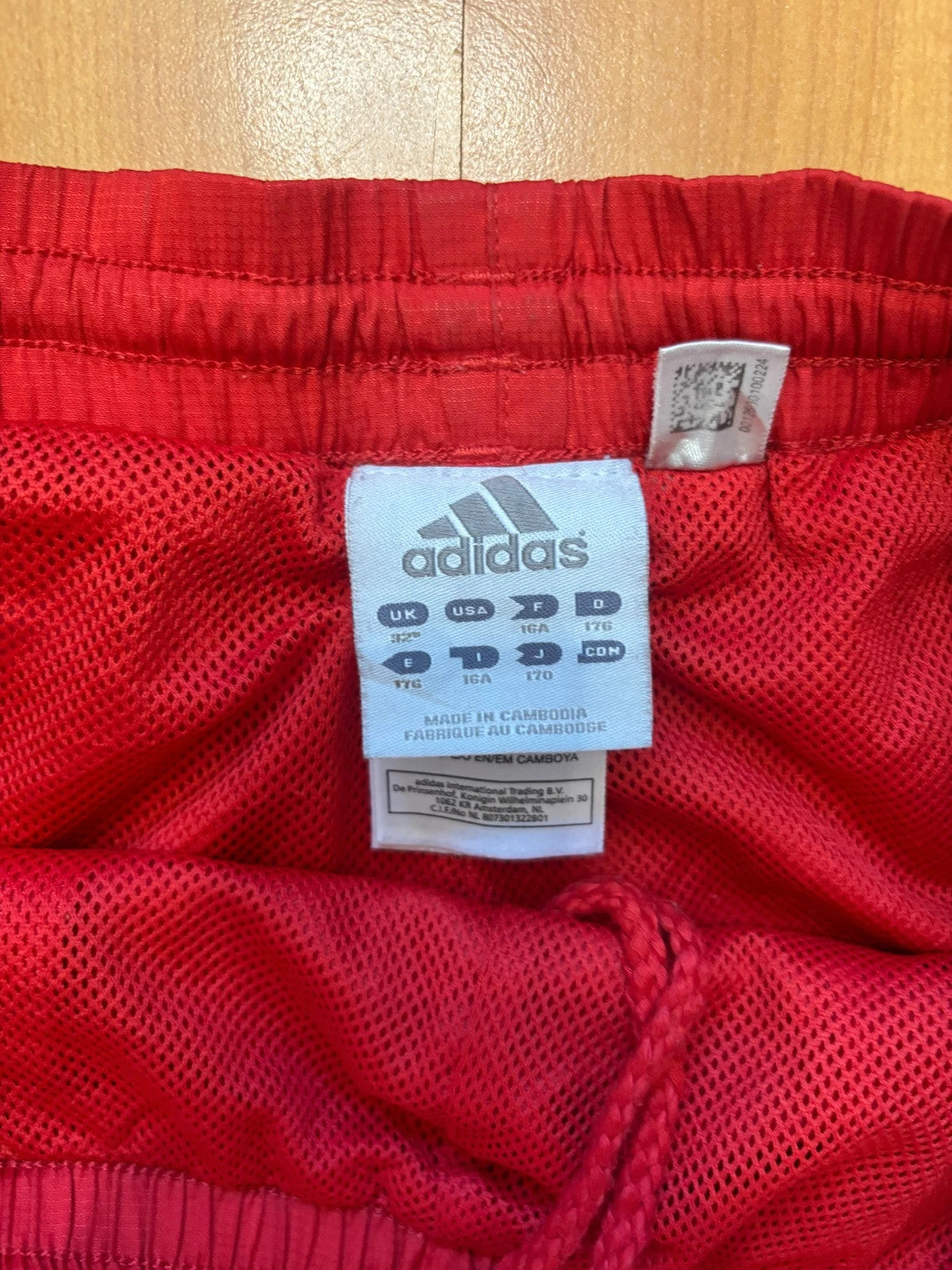 Adidas red joggers with white three-stripe detailing and adjustable drawstring waist.